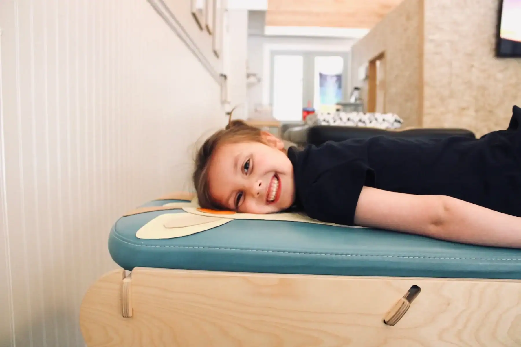 Photo of a young girl smiling while lying on a bench in a chiropractic clinic