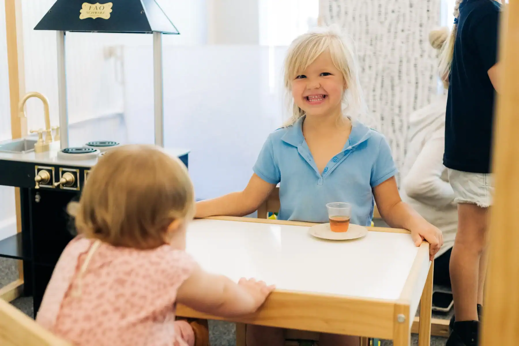 Photo of a young girl smiling while sitting at a table across from a young toddler depicting natural remedies for childhood anxiety