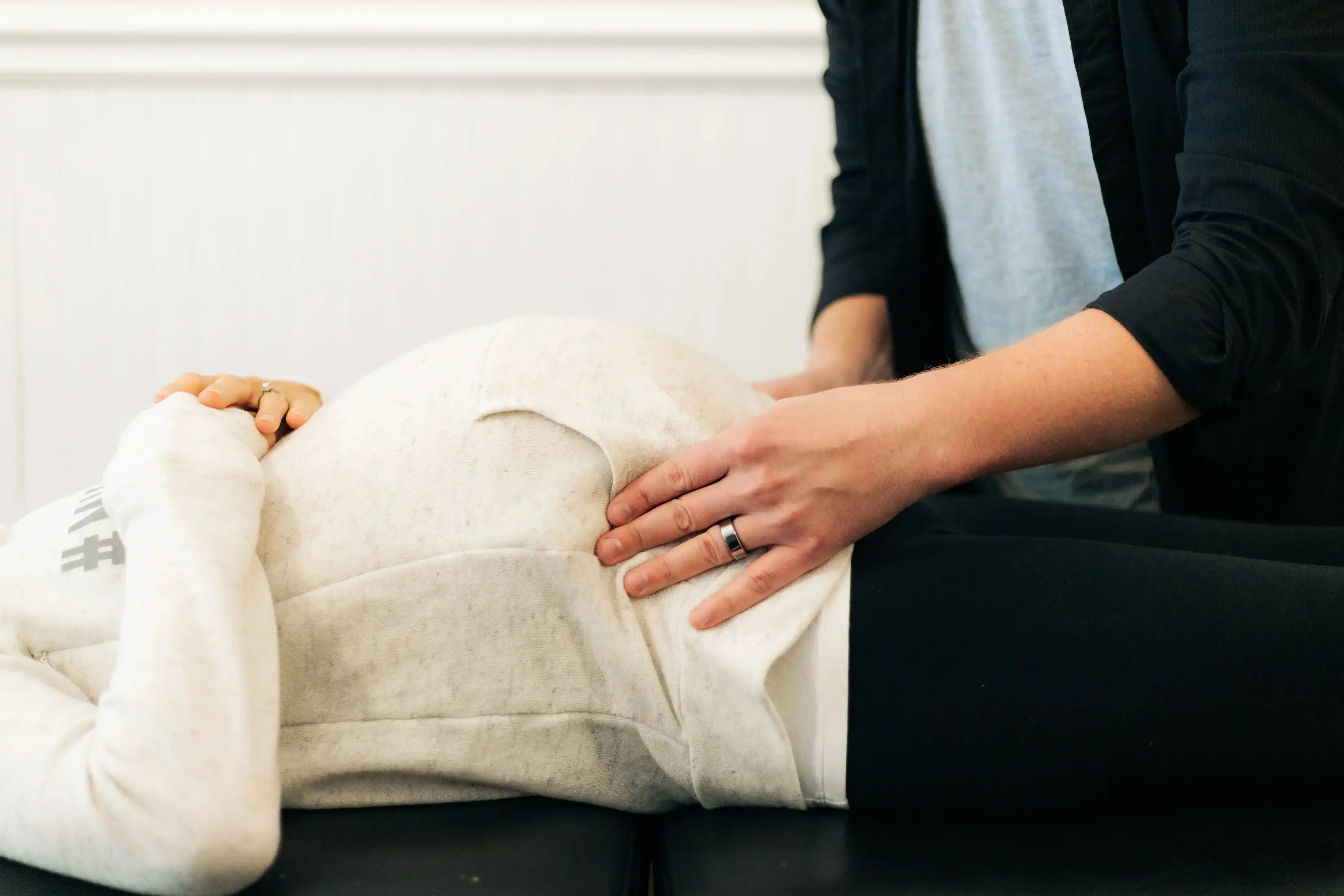 Photo of a Webster chiropractor placing his hands on a woman's pregnant belly while she is lying down to show how often should I go to the chiropractor while pregnant