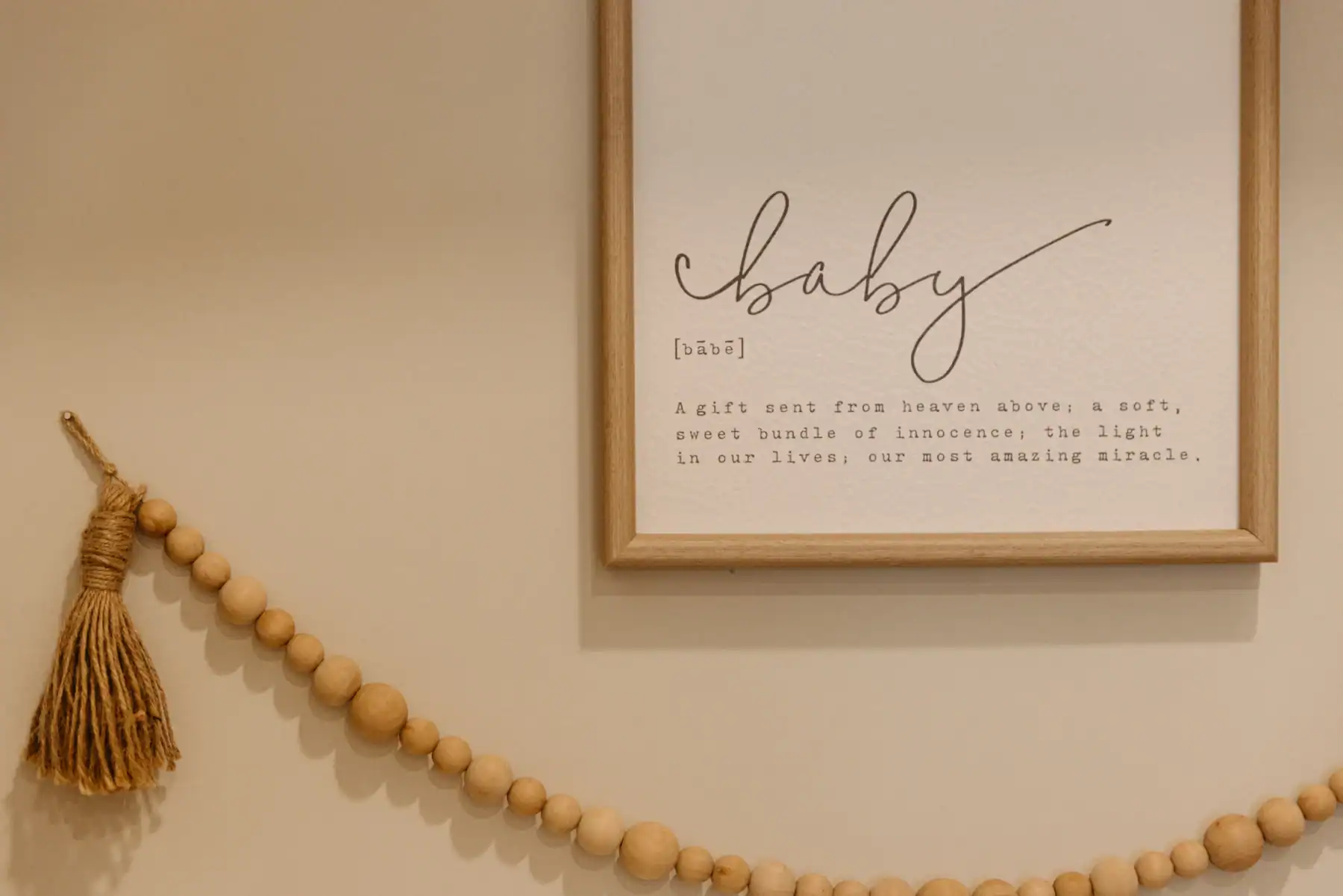 Photo of a hanged sign that says the definition of baby framed with wood above wood bead decor