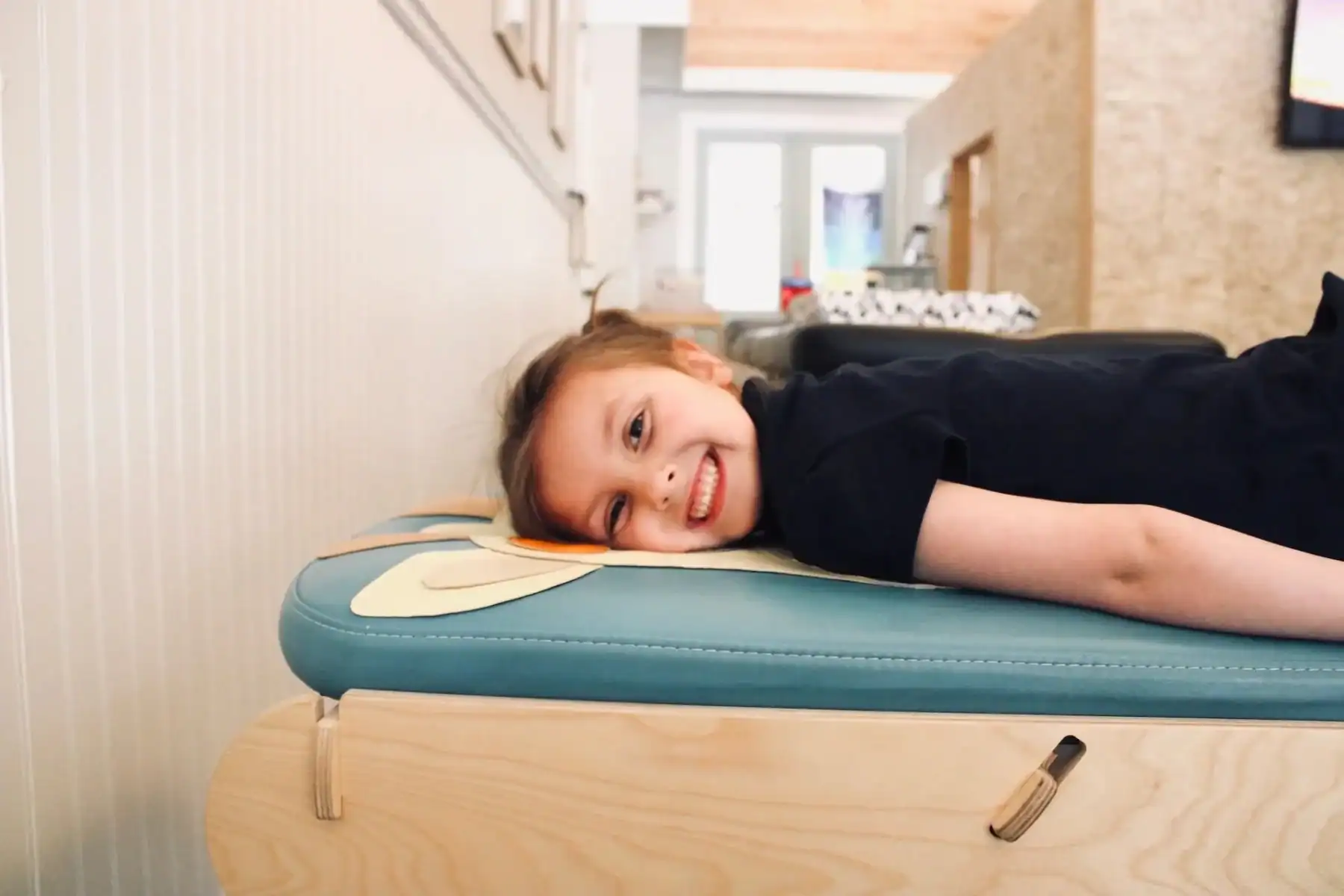 Picture of a smiling young girl lying on her stomach for her chiropractic care for subluxation on a blue chiropractic adjustment table in a bright clinic