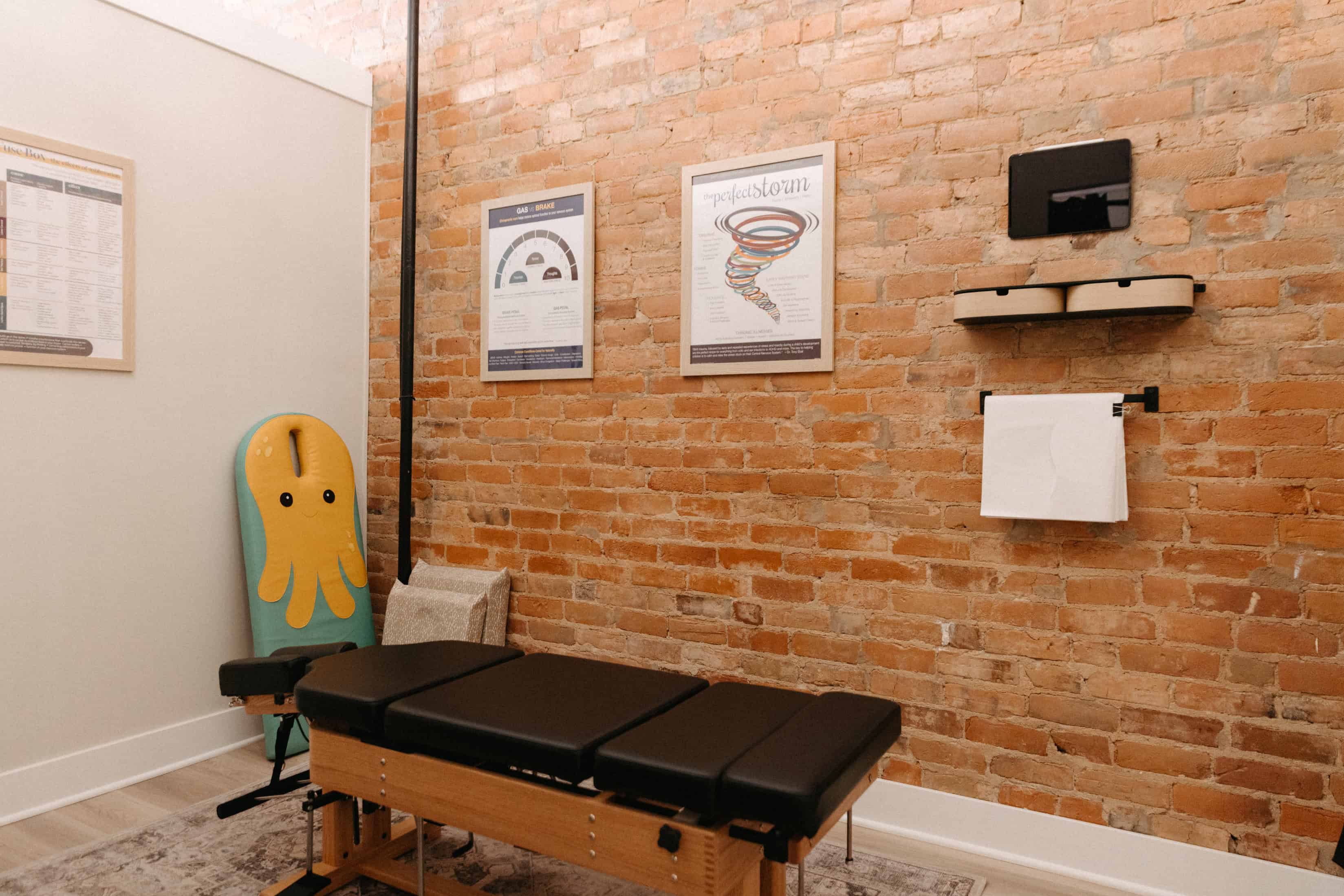 Photo of a nervous system chiropractor office with a black adjustment table in front of a brick wall