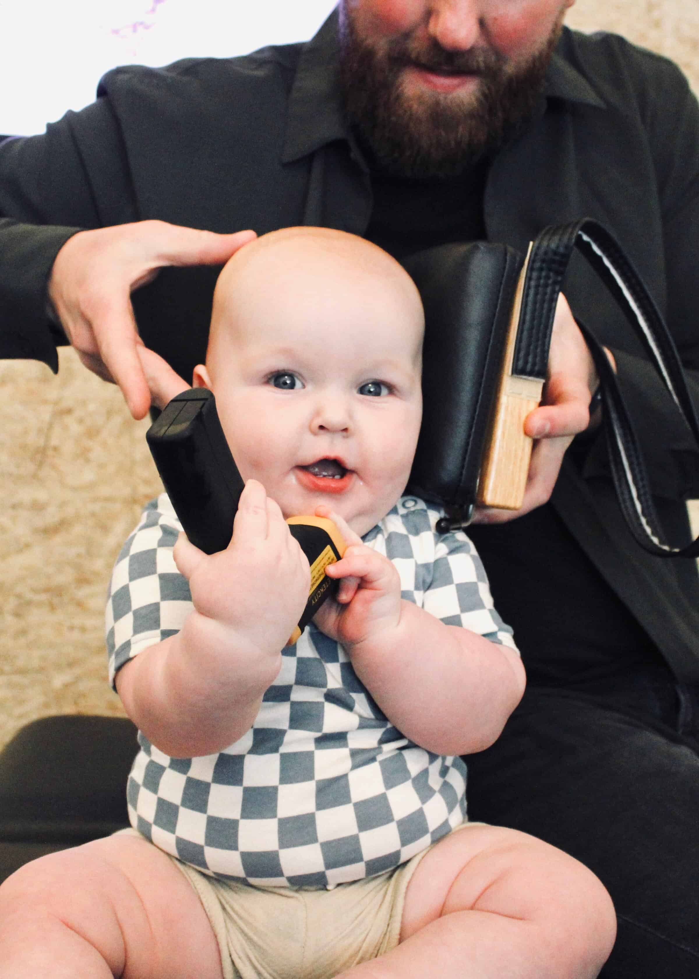 Picture of a happy baby sitting in a chiropractic office, demonstrating the natural immune support for kids while a practitioner gently holds neurological scanning equipment near the baby's head.
