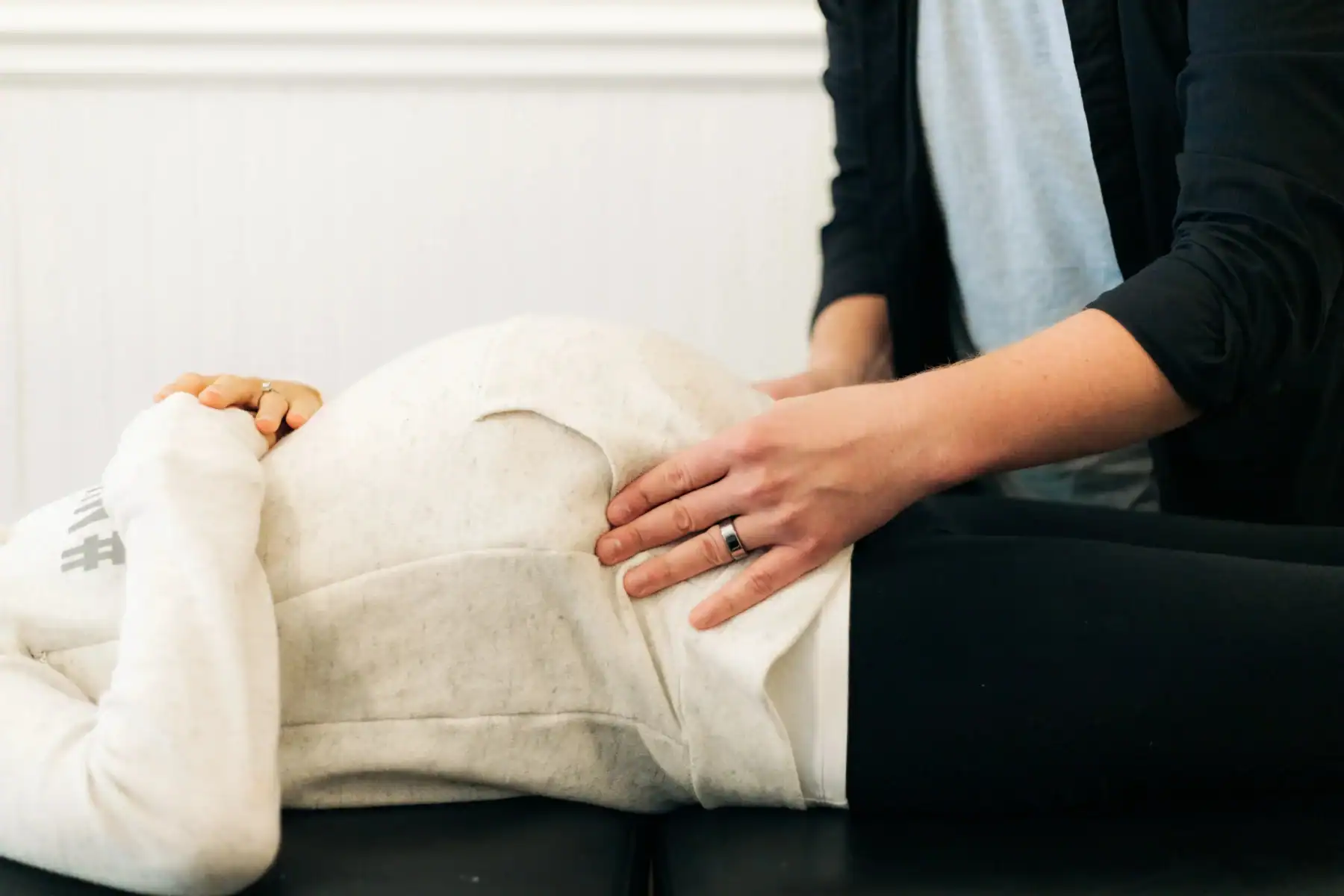 Photo of a doctor placing his hands on a woman's pregnant belly while she is lying down wondering "is it safe to see a chiropractor while pregnant?"