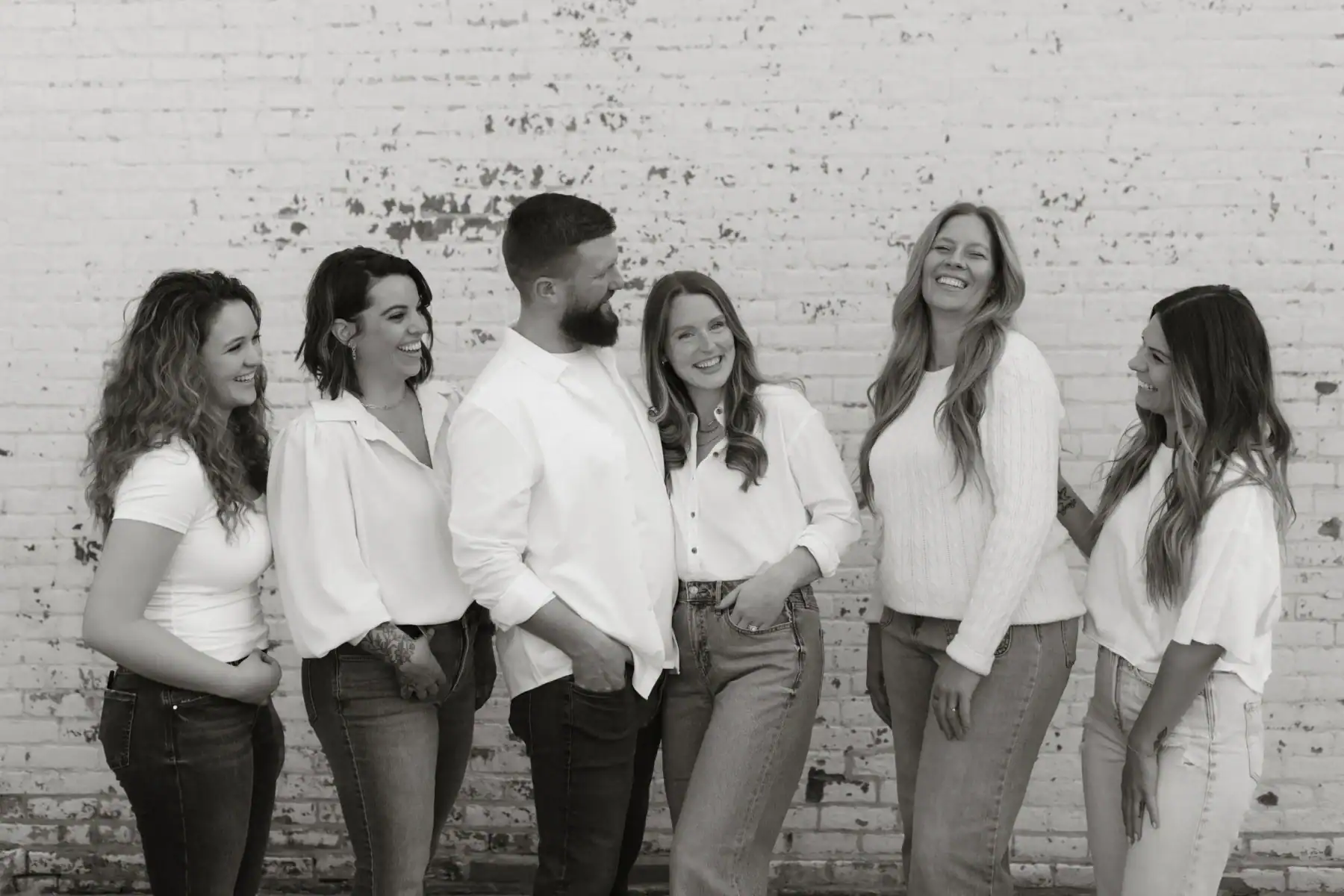 black and white photo of the Adjusted Living team 5 women and 1 man smiling together posing in front of a brick wall