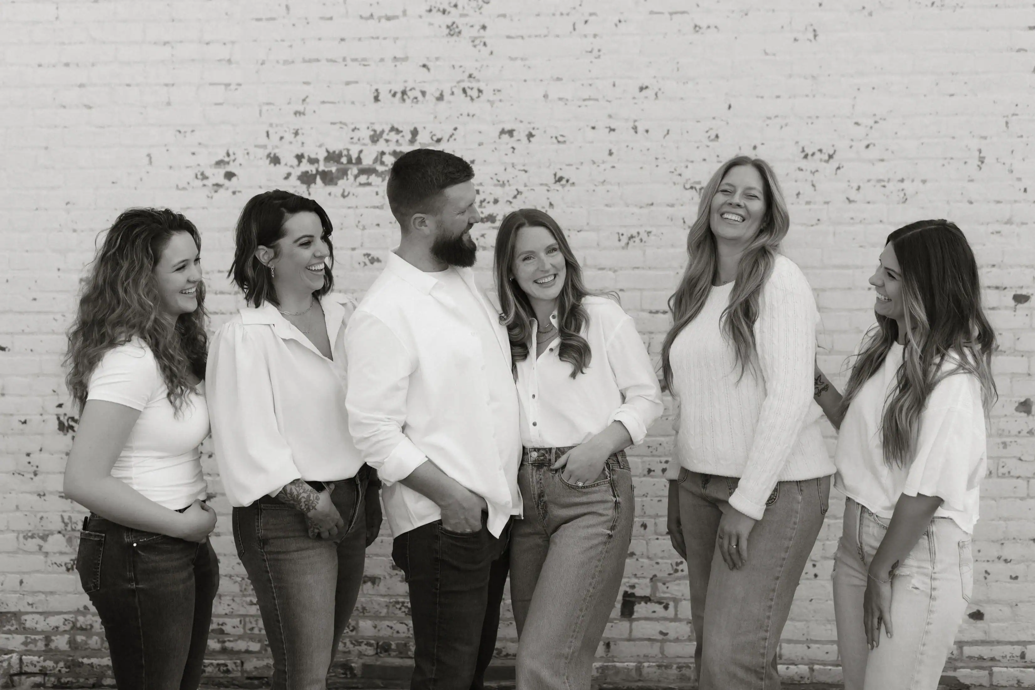 black and white photo of the Adjusted Living team 5 women and 1 man smiling together posing in front of a brick wall