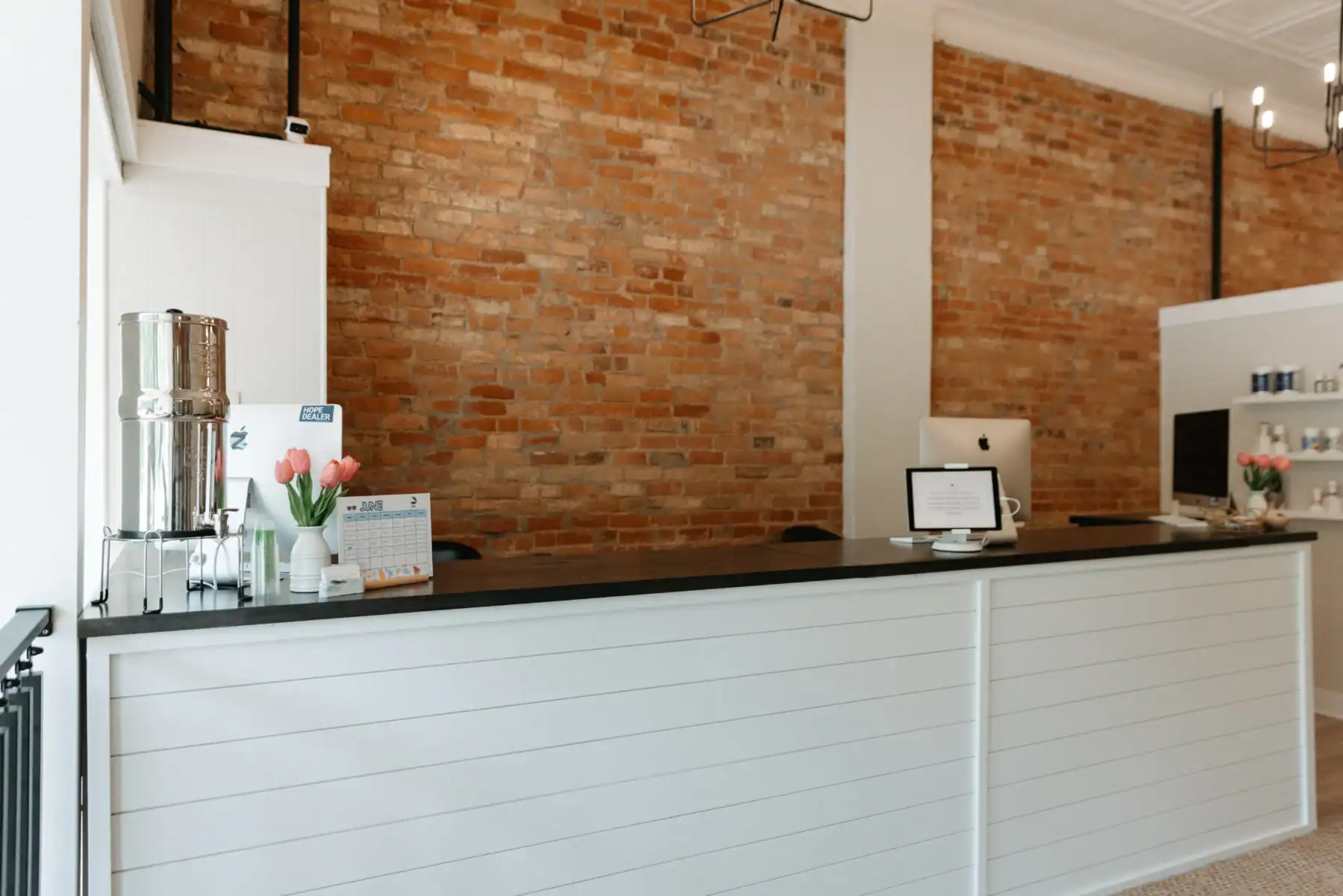 photo of a white front desk with Apple monitors for teens and technology plus other decor in front of a brick wall