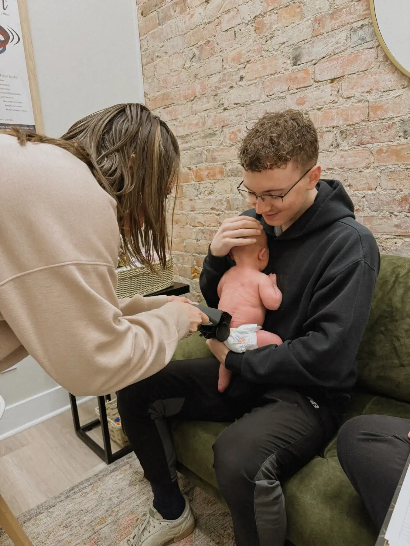 photo of a baby getting his back scanned by a woman as he sits in a man's lap