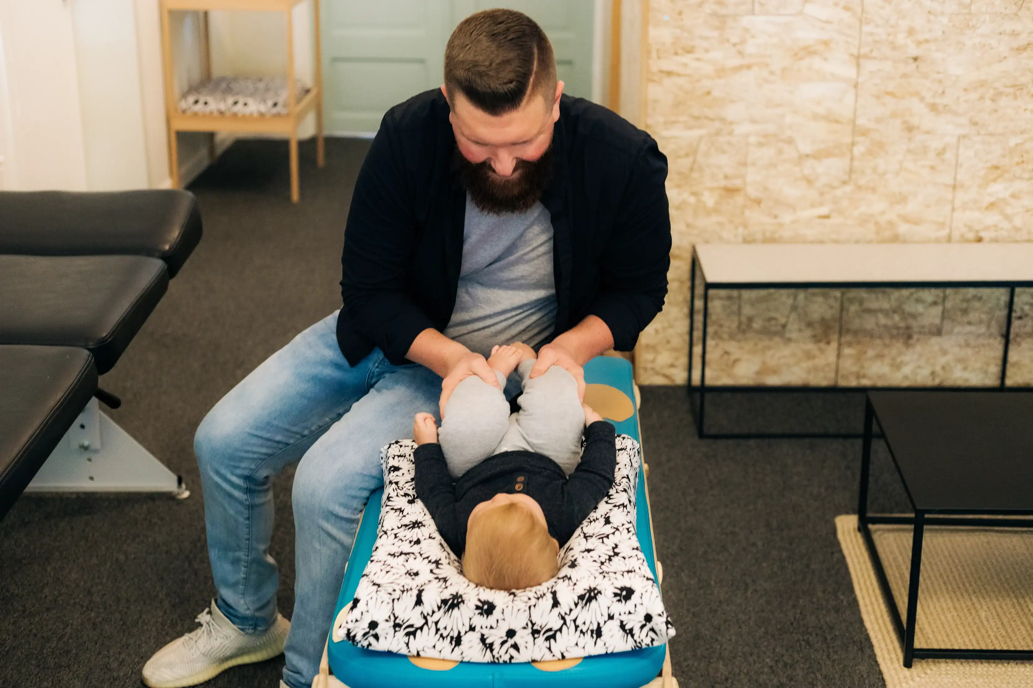 photo of a chiropactor lifting the legs of a young boy as he lies on a blue bench and white pillow for nervous system dysregulation symptoms