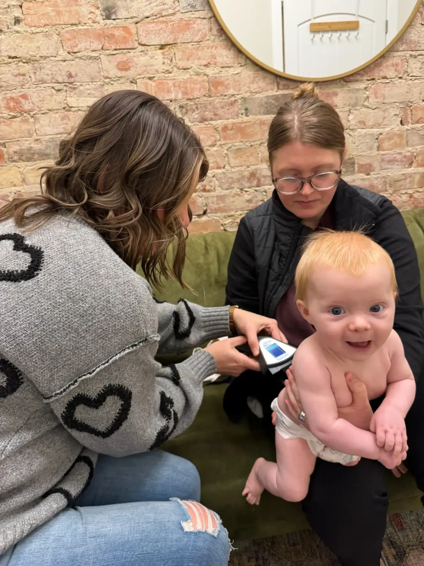 photo of a female chiropractor doing what is an INSiGHT scan on a baby boy as his mother holds him