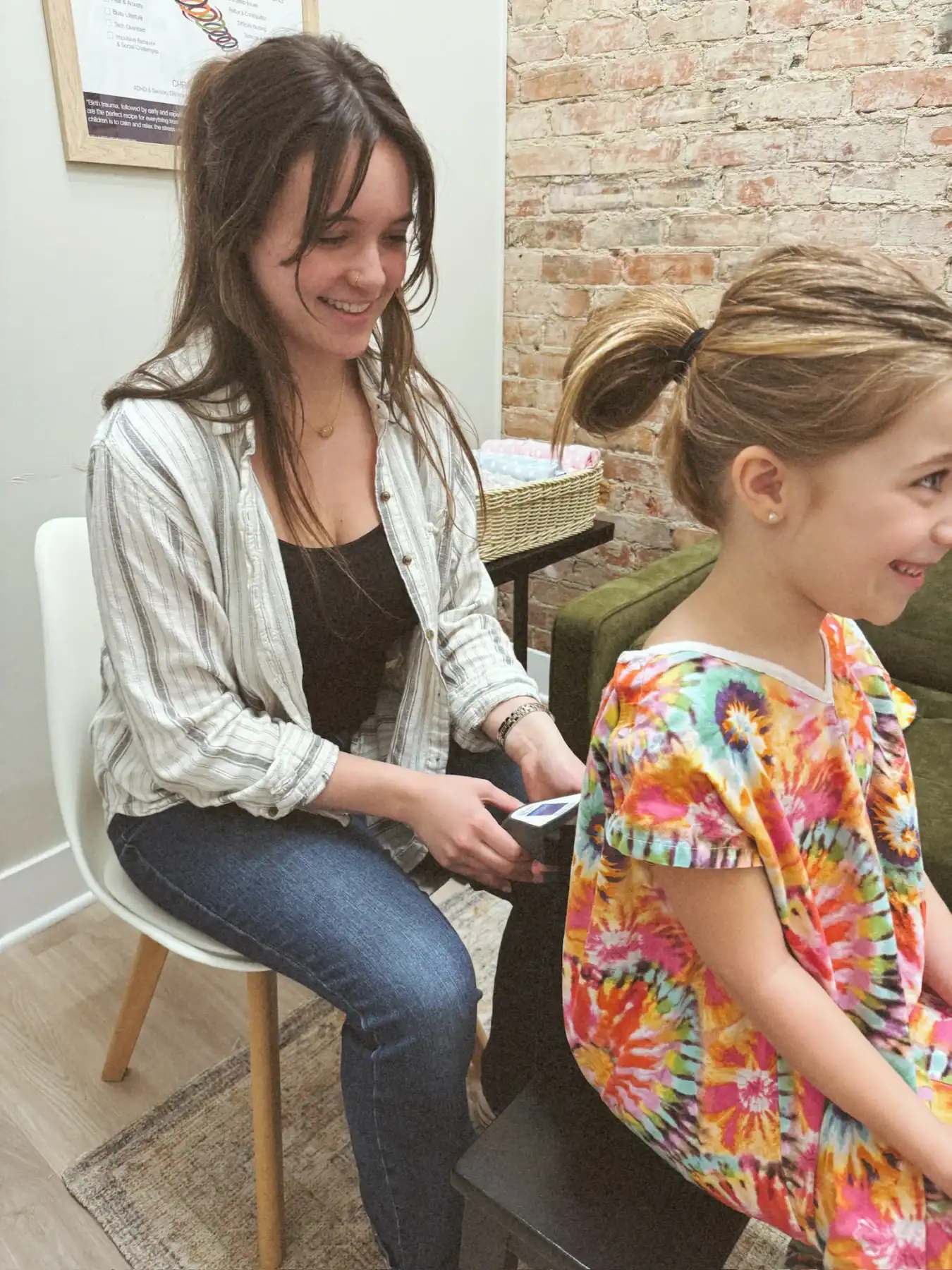 photo of a girl getting her back scanned by a woman as she sits in a patient robe smiling
