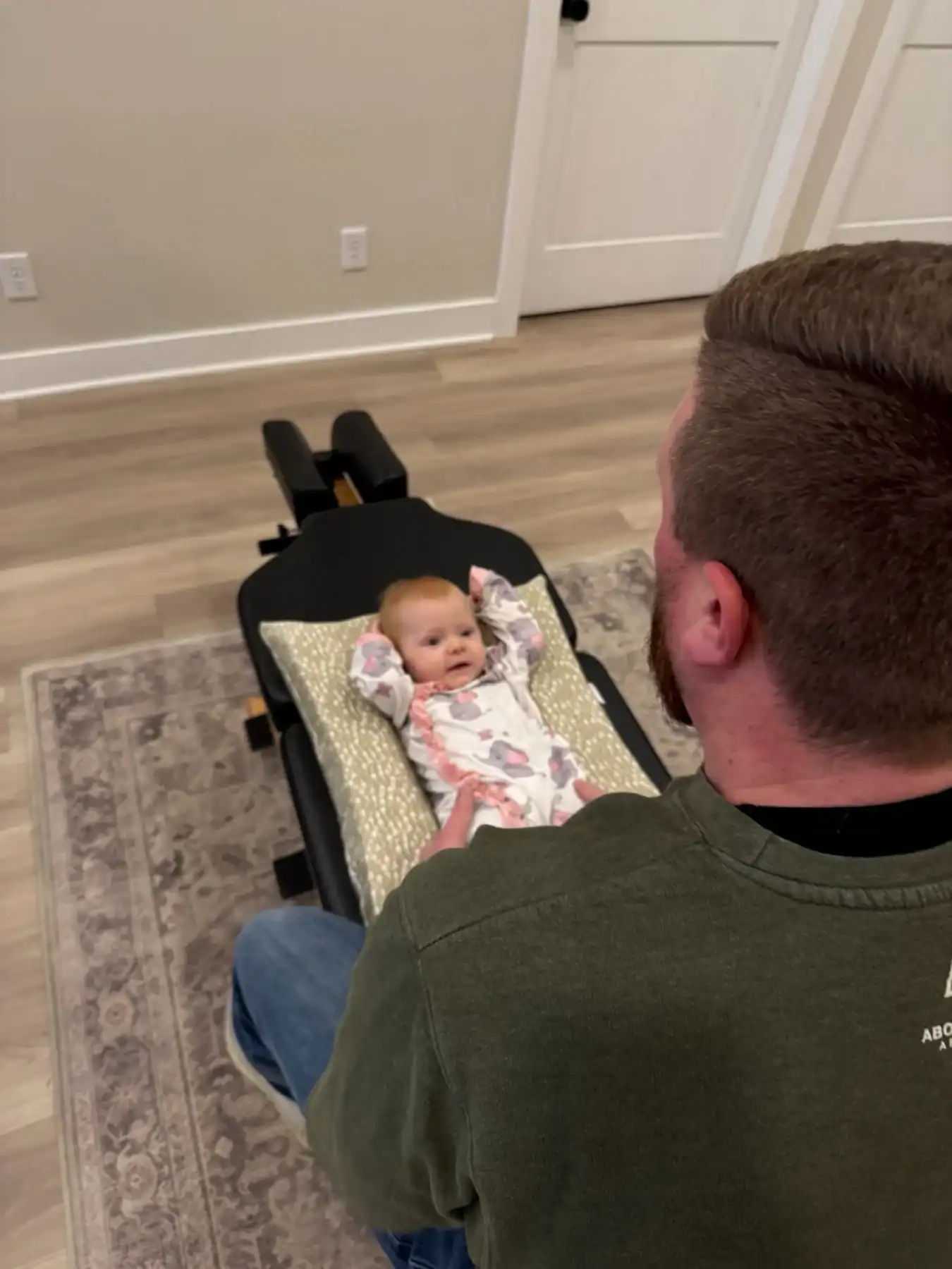 photo of a male chiropractor doing a baby chiropractic adjustment on a newborn baby laying on a bench