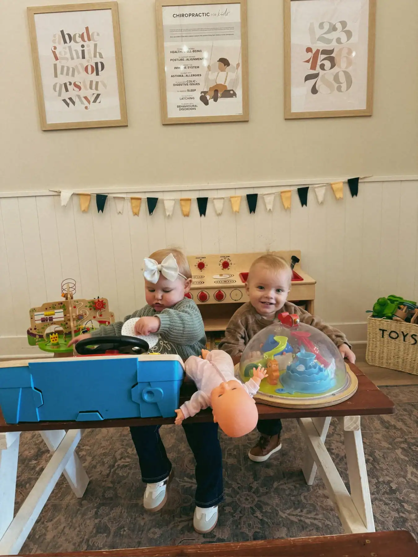 photo of a young girl and boy playing with toys together on a wood table in a chiropractic office