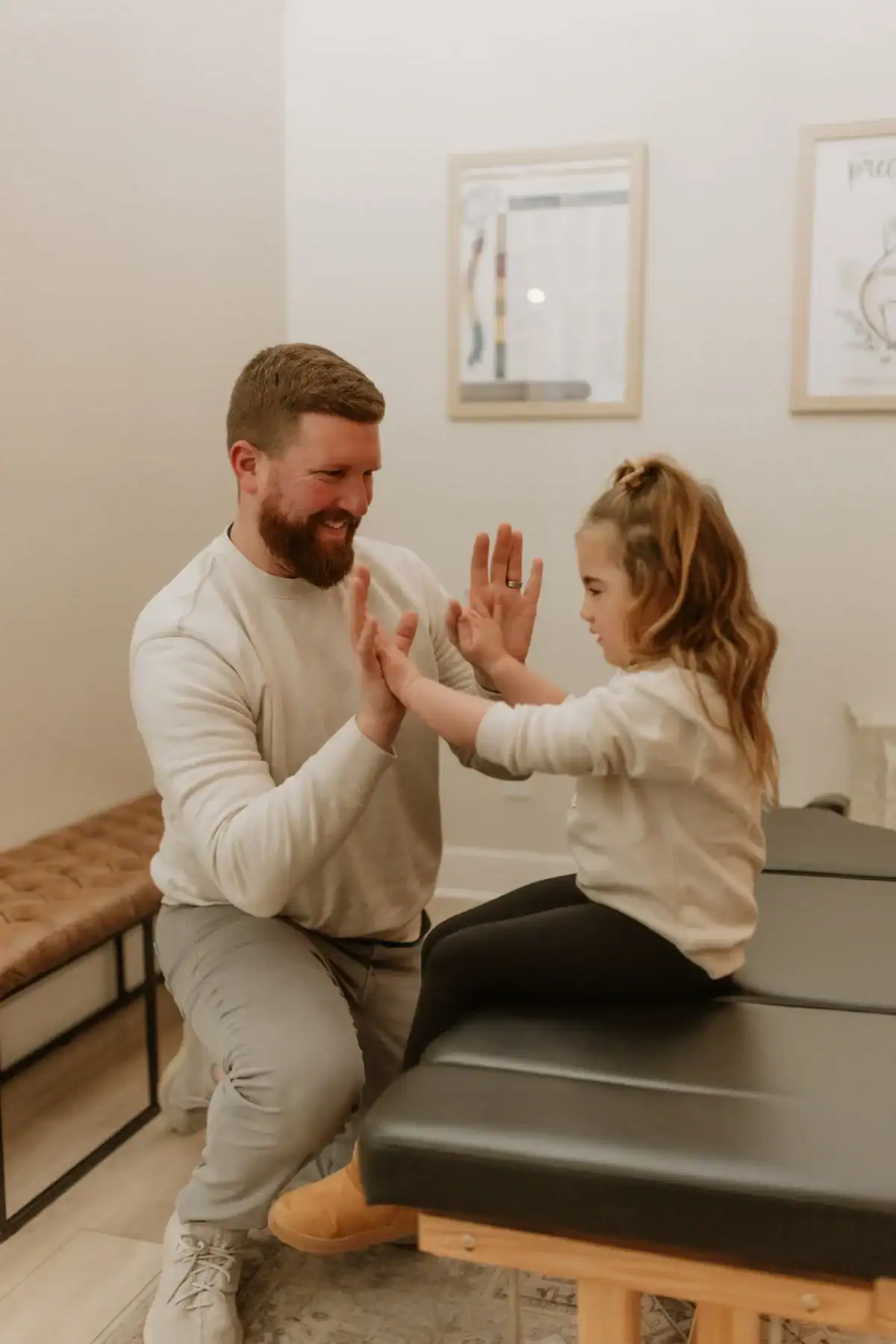 photo of chiropractor Dr. Ryan Angelo high-fiving a young girl as she sits on a black chiropractic bench in the Adjusted Living office