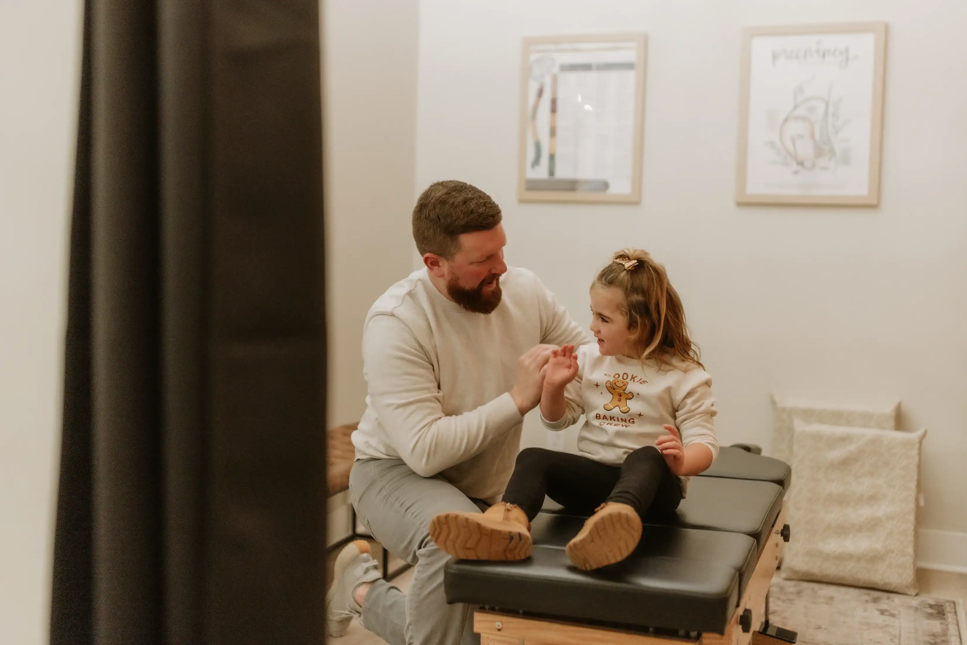 photo of male chriopractor adjusting a young girl's back on a black bench representing signs your nervous system is healing