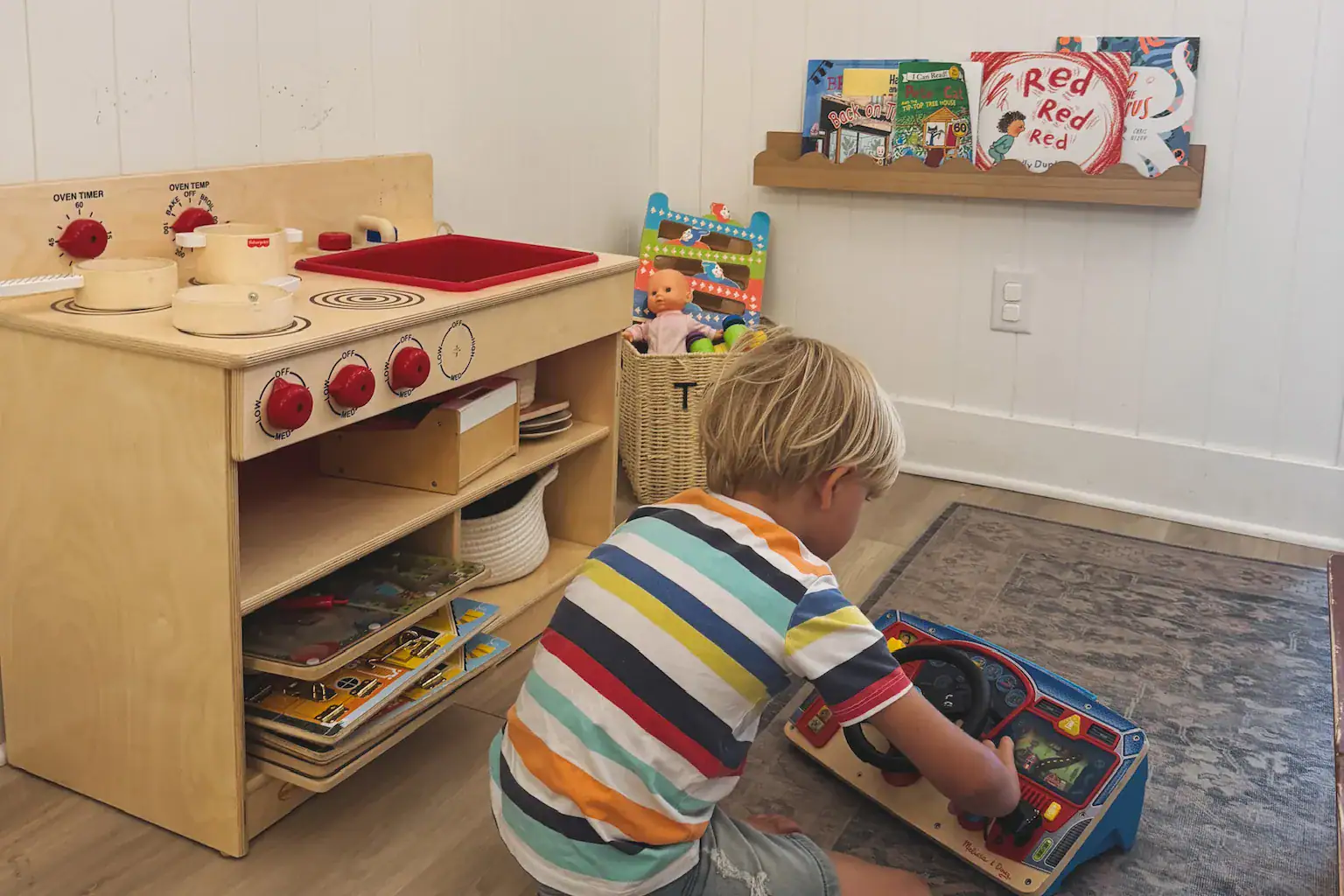 photo of a young boy playing with a toy car in a kids play area with a play kitchen