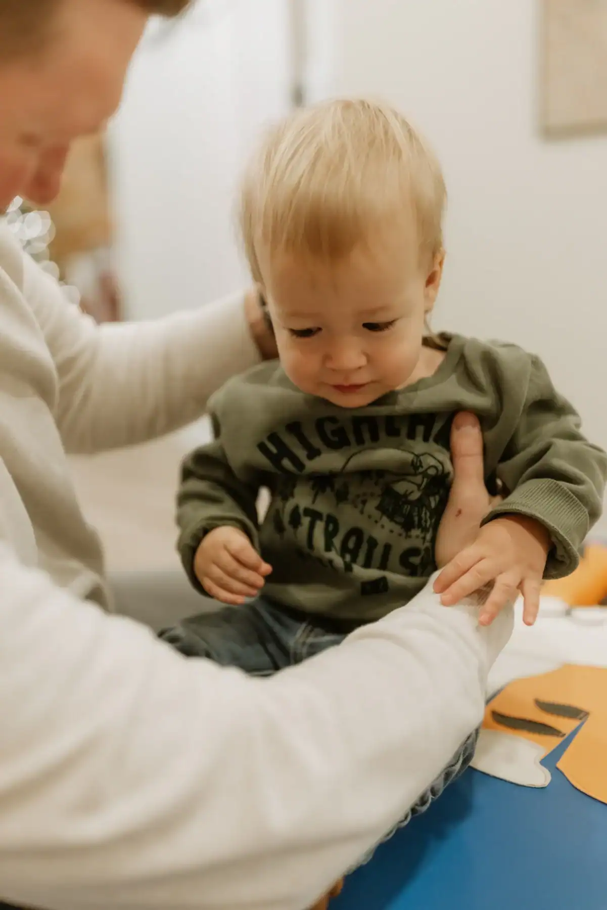 photo of a young boy sitting on a blue chiropractor bench held by a parent wondering why does my child keep getting ear infections